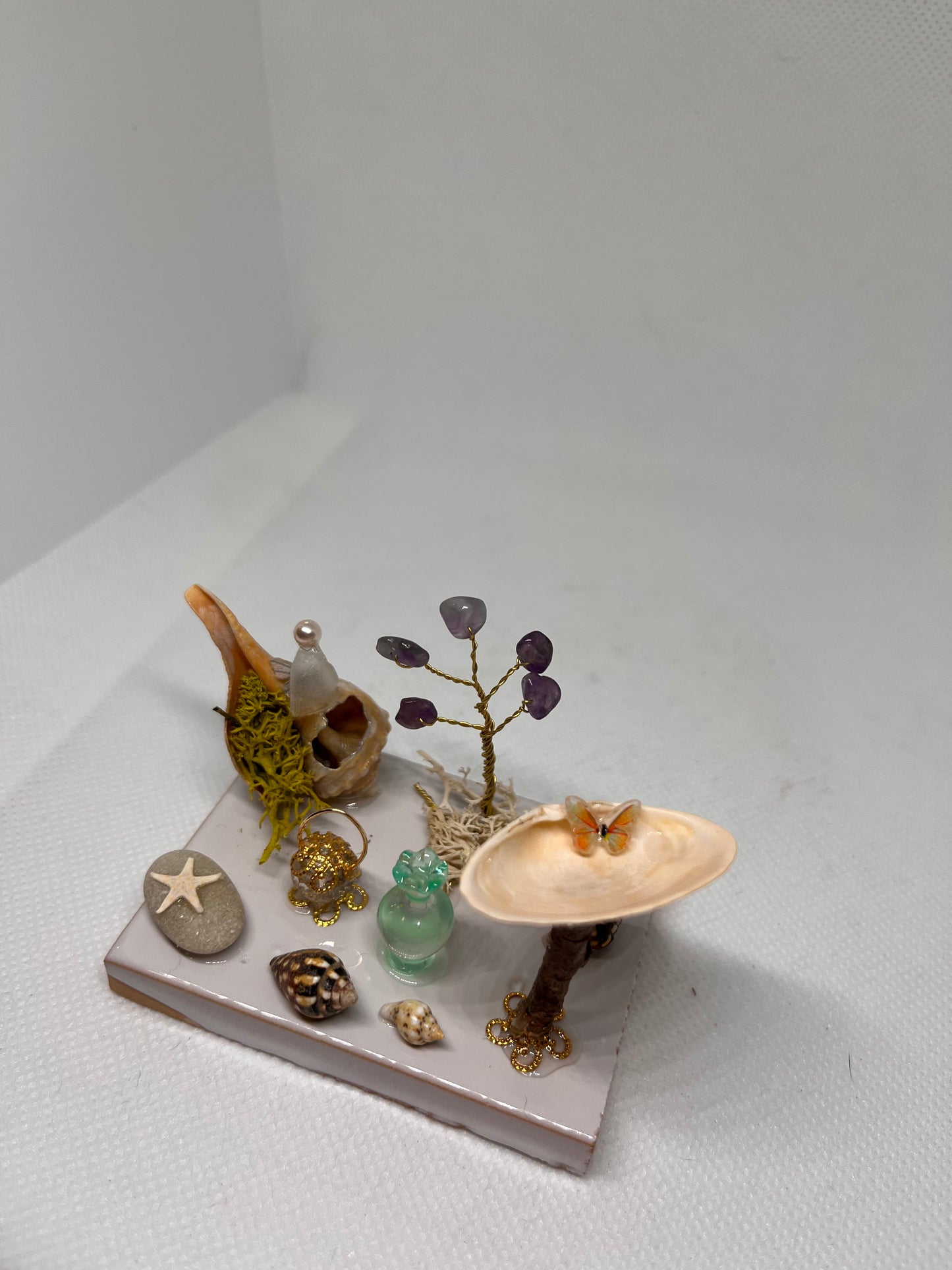 White Sea Glass Fairy Cottage Conch Shell w/ Bird Bath, Lantern, Vase, and Amethyst Tree on White Tile